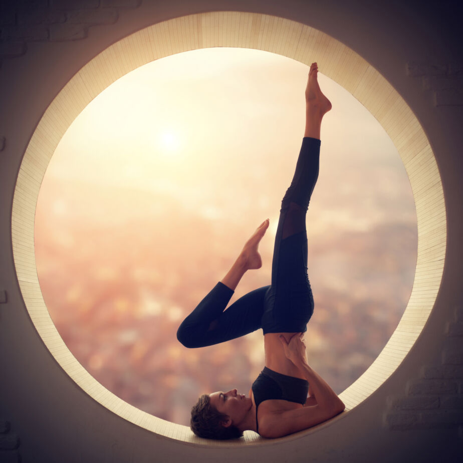 beautiful sporty fit yogi woman practices yoga salamba sarvangasana shoulderstand pose in a window