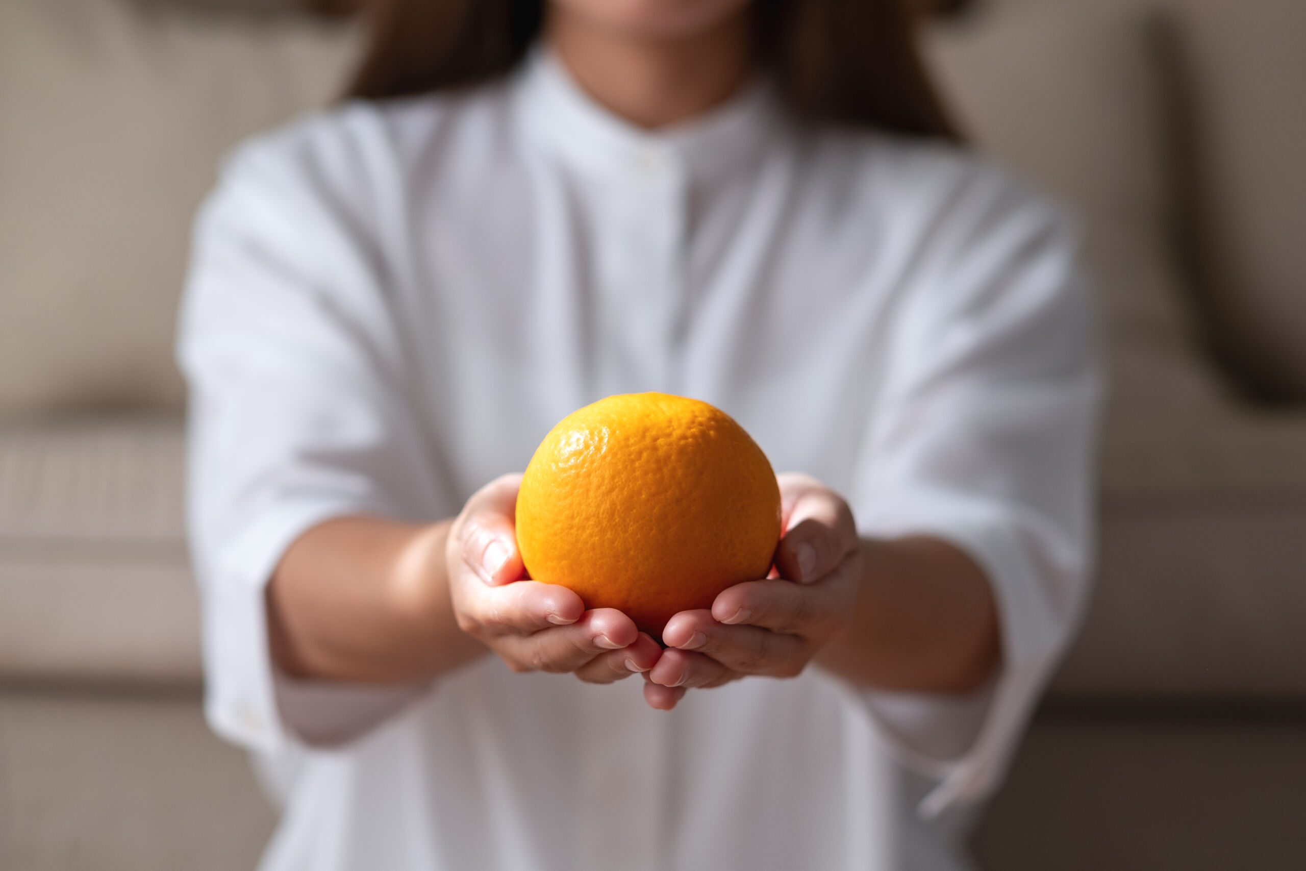 closeup image of a young woman holding and showing an orange